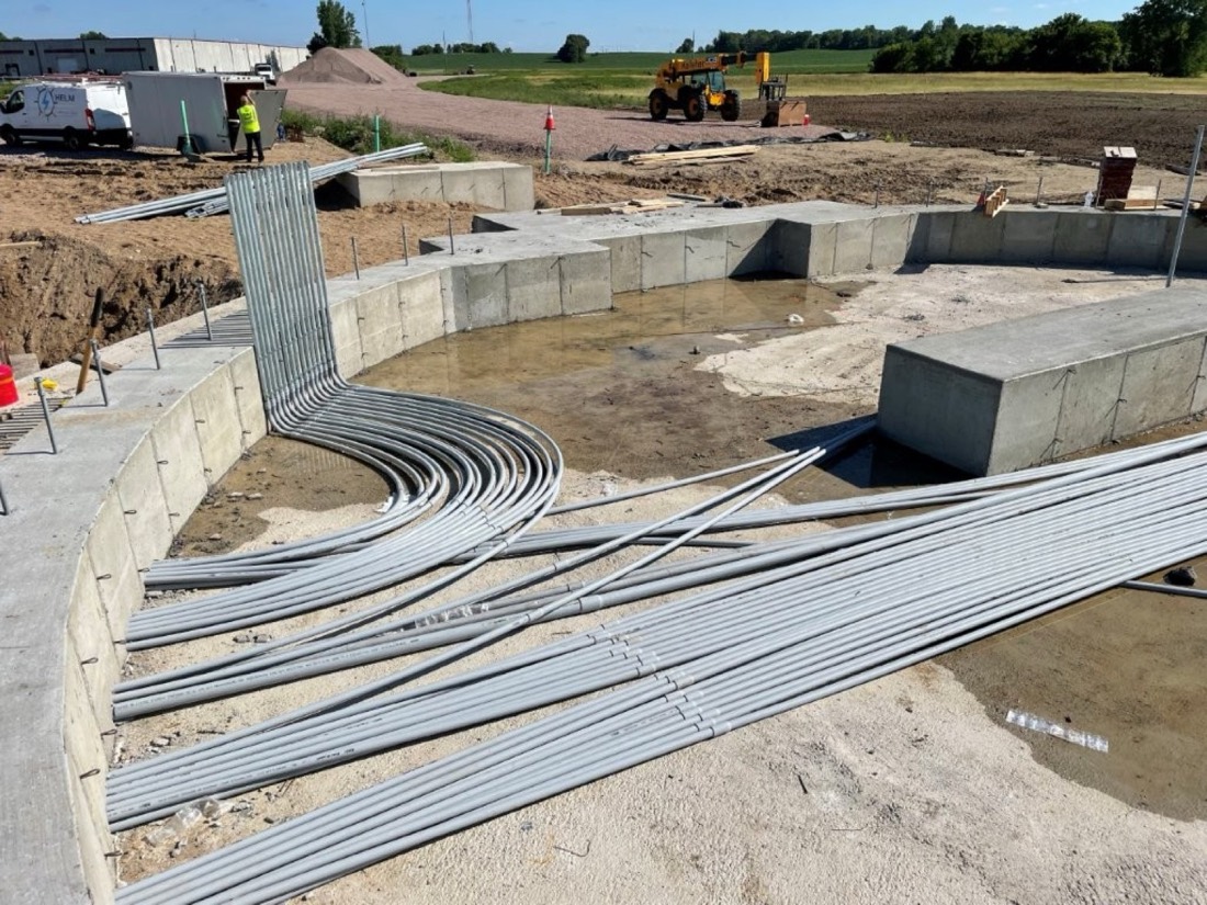 A wide bank of conduit sweeping out of a poured concrete foundation wall before backfill.